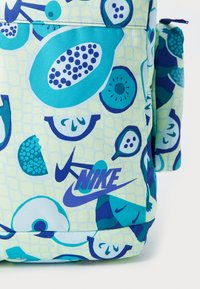 Fargerik ryggsekk med en lys gul bakgrunn og forskjellige fruktmønstre i blå og grønne nyanser. Inkluderer en fremtredende Nike-logo.