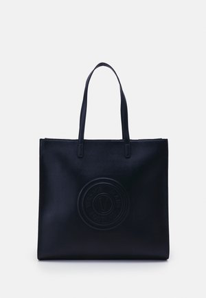 Zwarte totebag met twee lange hengsels en een circulair reliëflogo met de tekst Versace Jeans Couture aan de voorkant in het midden.