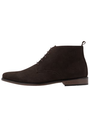 Bottine homme en daim marron foncé avec lacets, languette au talon et semelle basse en bois empilé.
