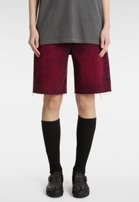 Shorts de mezclilla rojos con dobladillos deshilachados, combinados con calcetas negras hasta la rodilla y zapatos negros con tachuelas. La parte superior es una camiseta gris holgada.