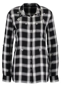 Chemise à manches longues à carreaux noir et blanc, boutonnée, avec des ornements floraux en perles sur la poitrine et le col.