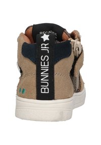 Tan suède sneakers met een gestructureerd ontwerp, marineblauwe accenten, witte zool en een zwarte band met "BUNNIES JR" in het wit gedrukt.