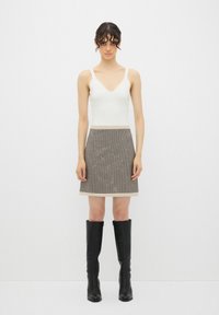 Top blanco sin mangas con cuello en V, combinado con una falda corta estampada en tonos beige y marrón, complementada con botas altas negras.