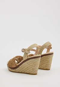 Sandalias de cuña con parte superior de tejido beige y marrón trenzado, correa de tobillo ajustable y un tacón de yute trenzado y texturizado.