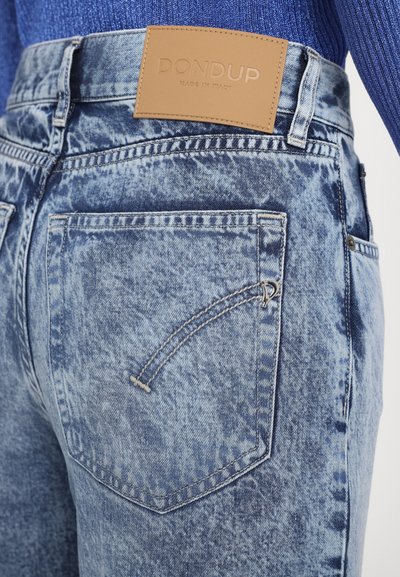 Denim jeans with a faded blue wash, featuring a tan leather waistband label. Back pocket includes a subtle curved stitch detail.