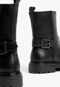Zwarte leren enkelboots hebben een ronde neus, een verstelbare gespaccent en een robuuste rubberen zool met groeven voor grip.