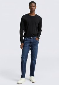 Must pika varrukaga särk, mida on kombineeritud siniste teksapükstega. Modell kannab valgeid vabaajajalatsid, väljendades juhuslikku stiili klassikalise siluetiga.