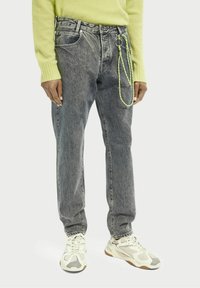 Szare jeansy z denimu o zwężanym kroju, ozdobione żółtym łańcuchem z linki i klasycznym fasonem z pięcioma kieszeniami. Stylizowane z jaskrawozielonym swetrem.