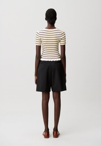 Top de manga corta a rayas en crudo y azul marino, con textura acanalada, combinado con pantalones cortos negros de tiro alto. Sandalias planas marrones completan el conjunto.