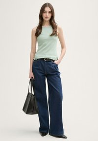 Top de tirantes de color verde claro con relieve, combinado con unos vaqueros de pierna ancha de mezclilla oscura, completado con un cinturón negro y un pequeño bolso negro.