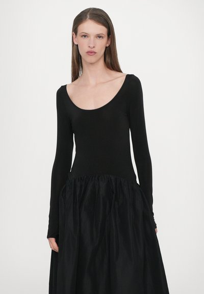 Vestido negro de manga larga con un corsé ajustado, escote redondeado y una falda acampanada, hecho de una tela ligera y texturizada.