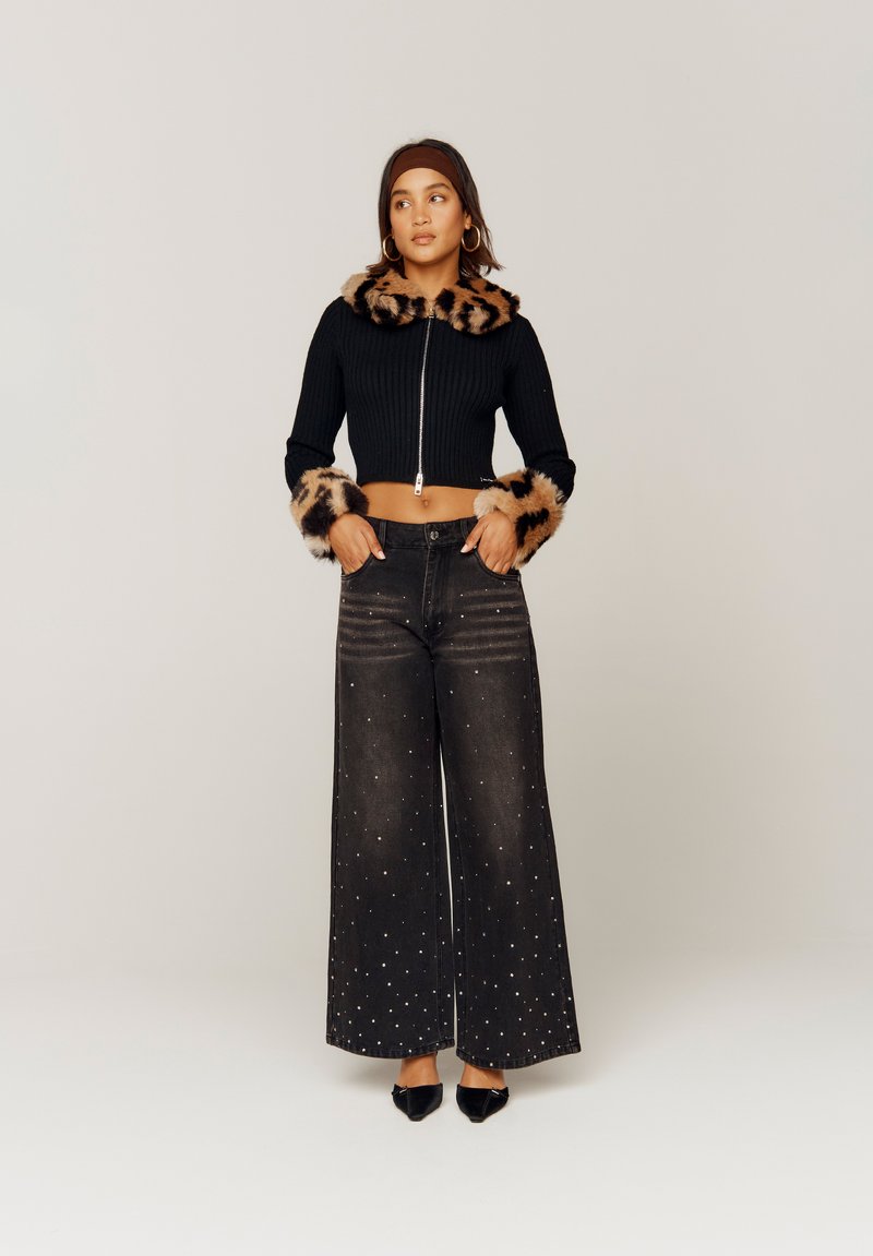Maglione cropped a coste nero con colletto e polsini in pelliccia sintetica leopardata; jeans neri a gamba larga decorati con piccole borchie argentate.