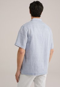 Camicia a maniche corte di colore azzurro chiaro, realizzata in tessuto testurizzato. Presenta un colletto e un motivo a righe delicate, progettata con una vestibilità rilassata e un giogo posteriore.