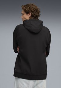 Chaqueta negra con capucha, fabricada con un tejido ligero y texturizado. Presenta una cintura ajustada y puños elásticos. Diseño sencillo sin estampados visibles.