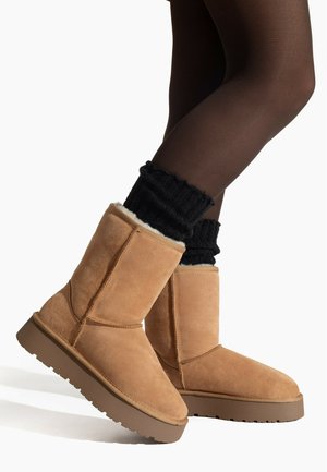 Tan suede ankle boots with a shearling lining, ribbed black socks peeking at the top, and a sturdy brown rubber sole.