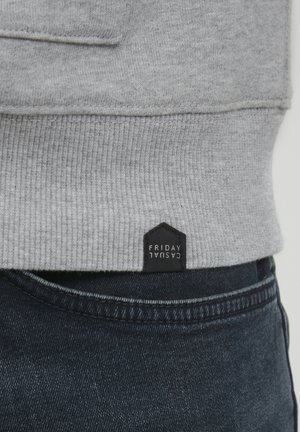 Gray sweatshirt with ribbed hem, featuring a black fabric tag labeled "FRIDAY CASUAL." Paired with dark denim jeans.