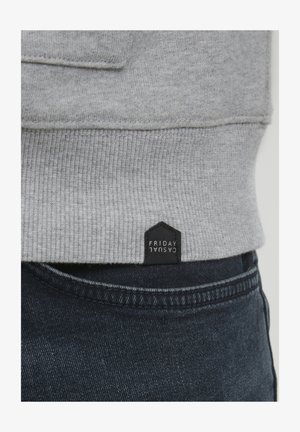 Gray sweatshirt with ribbed hem, featuring a black fabric tag labeled "FRIDAY CASUAL." Paired with dark denim jeans.