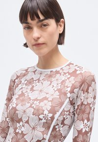 Long-sleeve rash guard in light brown with white floral pattern. Features a round neckline and seamless design for comfort.