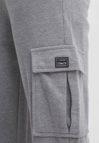 Gray fabric with a textured finish, featuring a side cargo pocket and a black label with "11 PROJECT 20/20" on it.
