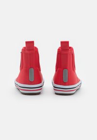 Une paire de bottes de chevilles imperméables rouges avec des patchs réfléchissants gris, des semelles blanches avec des rayures rouges et noires, vue de l'arrière.