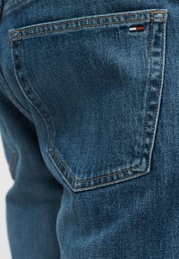 Τζιν denim με σκούρο μπλε χρώμα, πίσω τσέπη με αντίθετη ραφή και μικρό κεντητό λογότυπο σε κόκκινο, λευκό και μπλε.