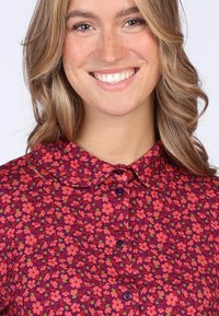 Collared shirt in purple fabric with a floral pattern in shades of pink and green. Features buttons and a textured finish.