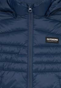 Veste matelassée bleu marine avec fermeture éclair à l'avant, capuche ajustable et une étiquette noire rectangulaire portant la mention "OUTDOORS Expedition."