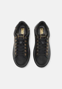 Crne kožne tenisice s zlatnim rupama i detaljima. Ravne vezice i glatka tekstura. Logo prikazan na ulošku. Okrogli oblik prsta.