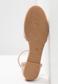 Sandale rose clair avec un dessus en daim doux, une fine bride et une semelle en caoutchouc texturée affichant un motif paisley. Taille indiquée comme 37.