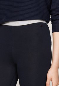 Marina leggings med en åtsittande design, tillverkade av stretchigt material. Har en vit midja med "TOMMY HILFIGER"-logotyp och en röd och vit logodetalj.