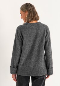 Grijze gebreide trui met een losse pasvorm, geribde manchetten en zoom. Zachte textuur, ronde hals en langere achterkant voor een ontspannen draagcomfort.