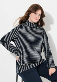 Marinblå och krämrandig turtlenecktröja med långa ärmar, i en lös passform och med sidofickor, matchad med mörka byxor.