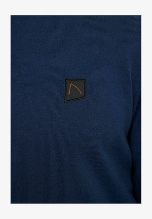 Suéter de punto azul marino con un acabado texturizado, que presenta un parche negro con un diseño geométrico naranja en el lado izquierdo.