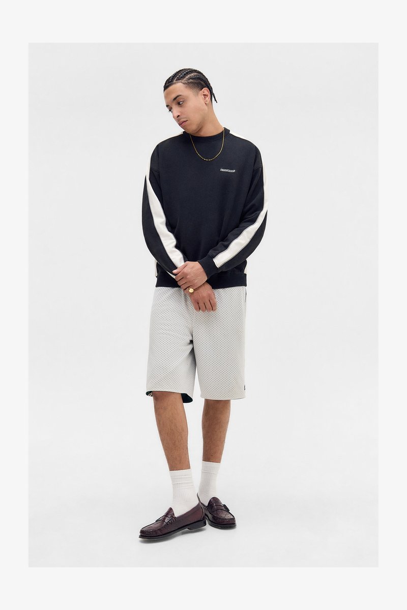 Schwarzer Hoodie mit weißen Seitenpanels, kombiniert mit hellgrauen perforierten Shorts. Braune Slipper und weiße Socken runden das Outfit ab.