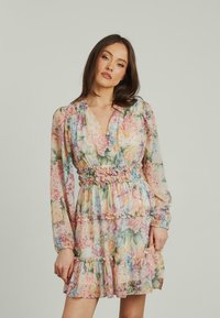 Blumengemustertes Kleid mit V-Ausschnitt, langen Ärmeln und Rüschenschichten. Hergestellt aus leichtem, transparentem Stoff in Pastellfarben. Elastischer Taillendetail.