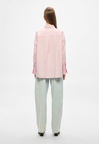 Camisa às riscas rosa claro com gola, mangas compridas e punhos abotoados, combinada com calças largas verde pálido. Textura do tecido lisa.