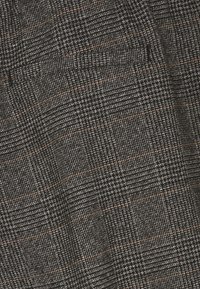 Tweed stof met een zwart en grijs ruitpatroon, voorzien van subtiele oranje lijnen. De textuur lijkt zacht en geweven.