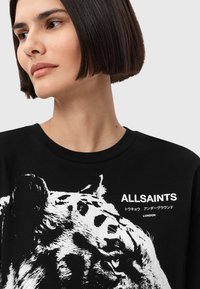 T-shirt in cotone nero con grafica di una tigre, testo bianco "ALLSAINTS" e dettagli di design, colletto a girocollo e maniche corte.