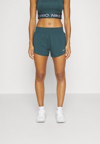 Pantalones cortos deportivos en color azul verdoso con cintura elástica, que presentan un pequeño logo blanco de Nike. Combinados con una camiseta corta a juego en azul verdoso con texto negro y reflectante.