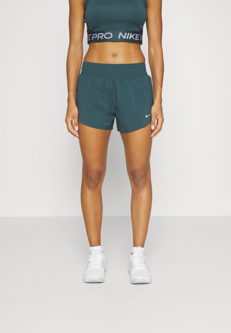 Pantalones cortos deportivos en color azul verdoso con cintura elástica, que presentan un pequeño logo blanco de Nike. Combinados con una camiseta corta a juego en azul verdoso con texto negro y reflectante.