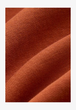 Close-up of folded burnt orange fabric showing soft texture and fine knit pattern.