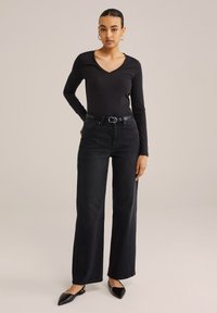 Juodas ilgomis rankovėmis V formos iškirptės viršus derinamas su juodomis aukšto liemens platesnėmis kelnėmis ir plokščiais smailiais bateliais. Papuoštas apvaliu diržo sagtimi.