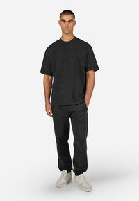 Sort oversized t-shirt med korte ærmer, parret med matchende sorte joggerbukser. Båret med hvide sneakers, fremvist mod en neutral baggrund.