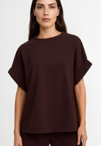 Maroon short-sleeve top in soft fabric with a relaxed fit, featuring rolled sleeves and a crew neckline. Simple, minimalist design.