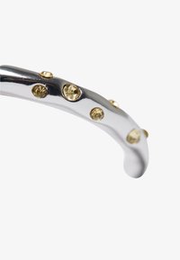 Sølvmetallarmbånd med en bølgende design, med innlagte gule rhinstein langs overflaten for dekorativt preg.