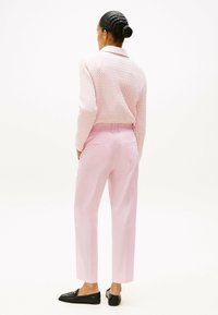 Lichtroze gebreide trui met een textuurpatroon en witte kraag, gecombineerd met op maat gemaakte roze broek en zwarte loafers, gezien vanuit de achterkant.