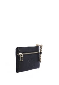 Bolsita de cuero negro con cierre de cremallera, logo circular grabado y una correa con patrón. Diseño compacto con textura suave.