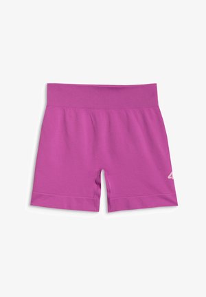 Młoda dziewczyna stoi, ubrana w fioletowy sportowy crop top i szorty z białymi skarpetkami i fioletowymi trampkami na szarym tle.
