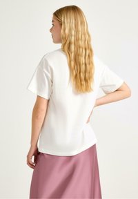 Hvid bomulds t-shirt med korte ærmer, afslappet pasform, buet nederkant. Båret med en pink satin skirt, der viser en glat tekstur og blød fald.