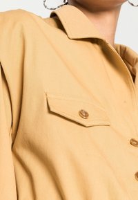 Lichtgele shirt met een kraag, een borstzak en knoopsluiting. Gladde stof met subtiele textuur en ronde knopen.